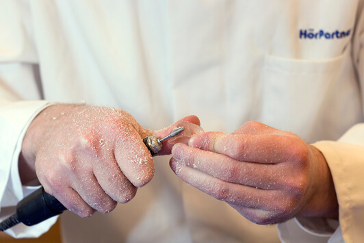 Ein Hörakustiker schleift ein Hörgerät präzise mit einer Fräse in der Werkstatt.